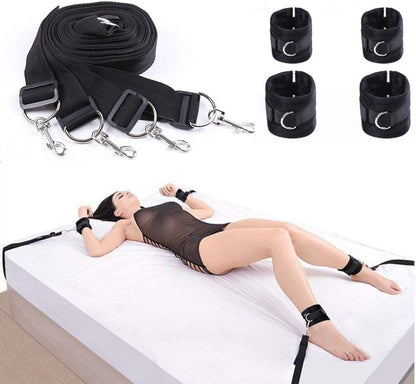 The image shows a person lying on a white bed with black under bed restraints attached to their wrists and ankles. The restraints appear to be made of nylon with metal rings, and there is a rolled-up black restraint lying beside the person.